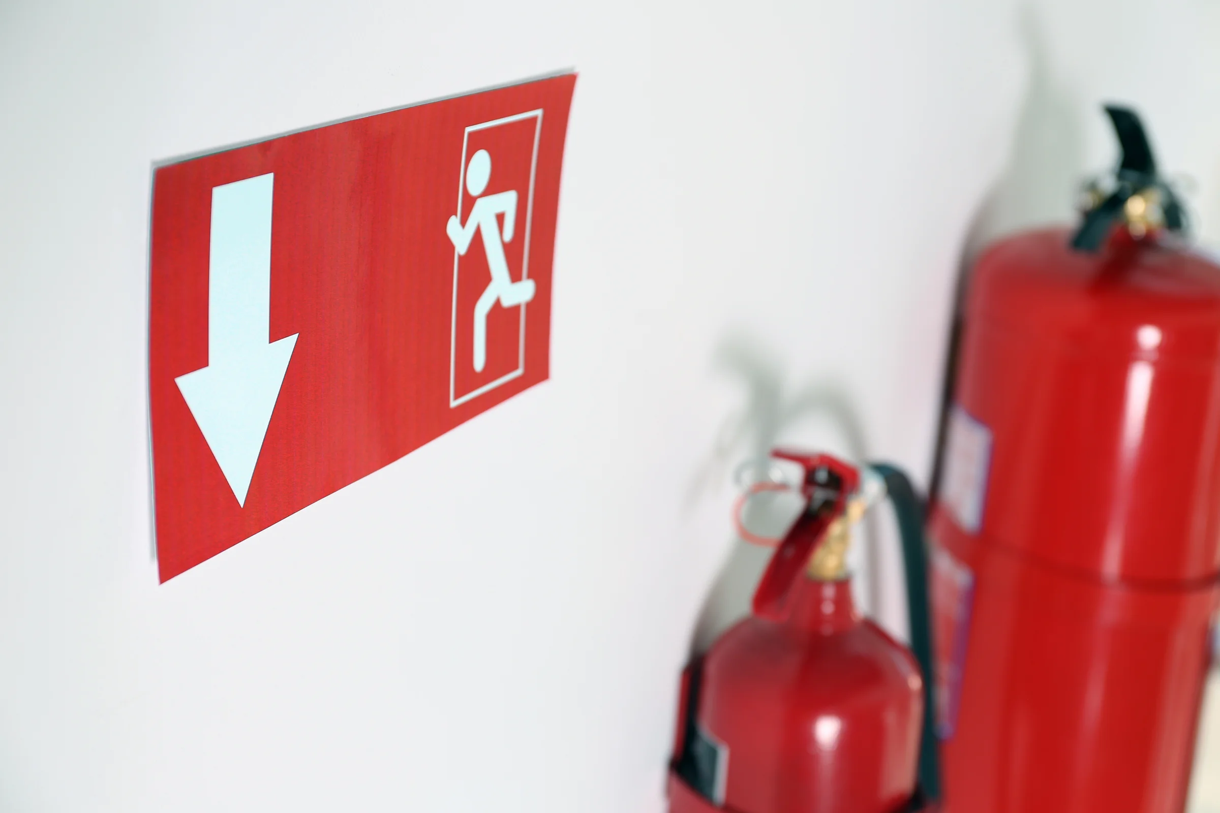Panneau d’issue de secours fléché fixé au mur, à côté de deux extincteurs